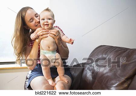 Stock Image - Caucasian mother holding baby daughter in armchair. Fotosearch
