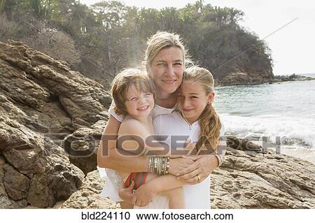 Stock Image - Caucasian mother hugging son and daughter at beach. Fotosearch