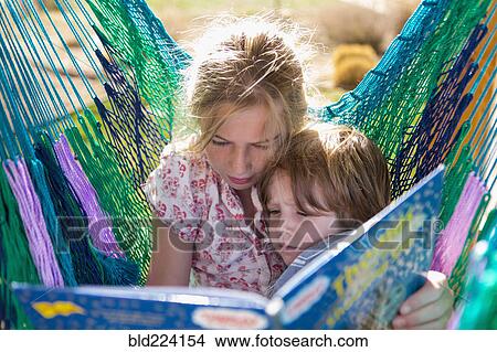Picture - Caucasian sister reading book to brother in hammock. Fotosearch