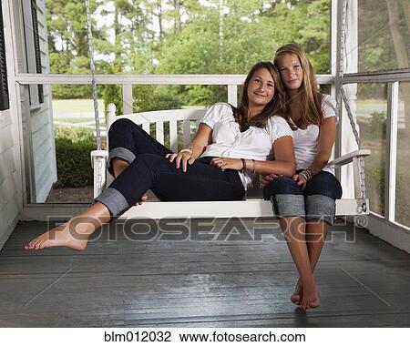 Stock Image - Caucasian sisters sitting on porch swing together. Fotosearch