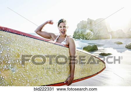 Stock Image - Caucasian surfer flexing muscle at beach. Fotosearch