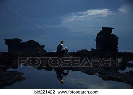 Stock Image - Caucasian teenage boy exploring rocky tidal pools at night, Canggu, Bali, Indonesia. Fotosearch