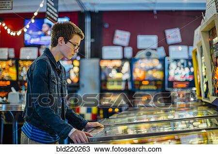 Stock Image - Caucasian teenage boy playing video game in arcade. Fotosearch