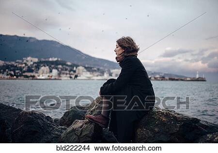 Picture - Caucasian woman admiring coastline from rock formation. Fotosearch