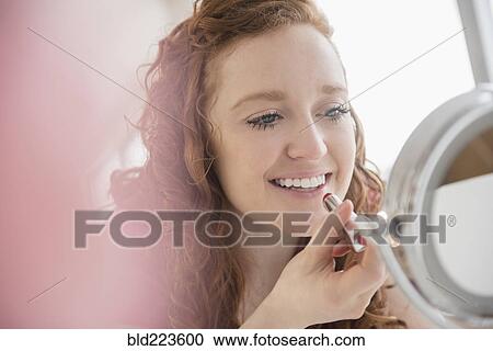 Stock Image - Caucasian woman applying lipstick in mirror. Fotosearch