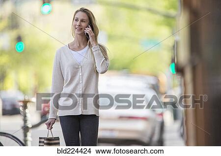 Picture - Caucasian woman carrying shopping bag using cell phone. Fotosearch