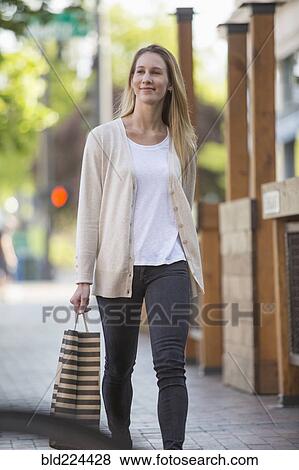 Stock Photo - Caucasian woman carrying shopping bag in city. Fotosearch