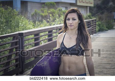 Stock Photo - Caucasian woman carrying skimboard on boardwalk. Fotosearch