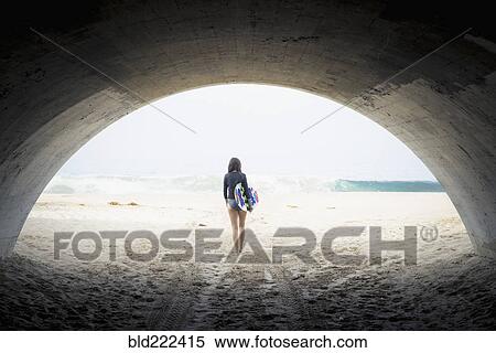 Stock Photography - Caucasian woman carrying skimboard under arch. Fotosearch