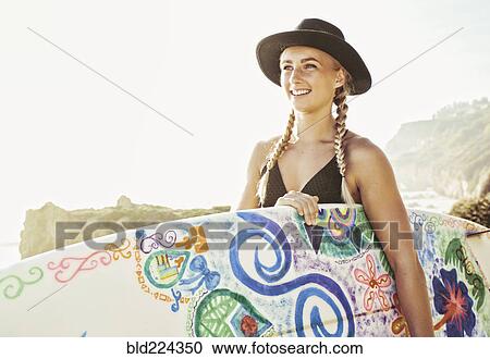 Stock Image - Caucasian woman carrying surfboard at beach. Fotosearch