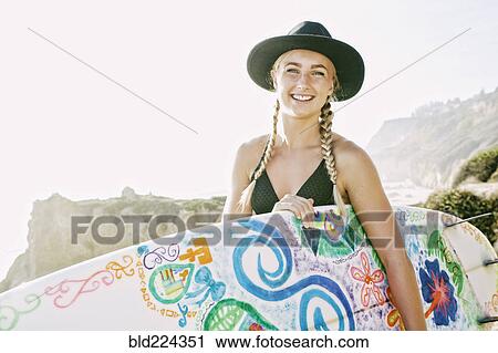 Stock Image - Caucasian woman carrying surfboard at beach. Fotosearch