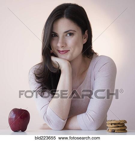 Stock Photography - Caucasian woman choosing between apple or cookies for snack. Fotosearch