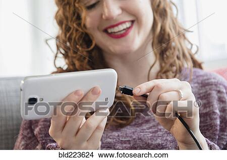 Picture - Caucasian woman connecting cord to cell phone. Fotosearch
