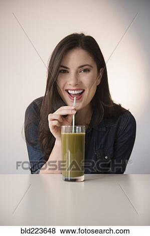 Stock Photo - Caucasian woman drinking green smoothie with straw. Fotosearch