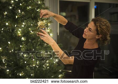 Stock Image - Caucasian woman hanging ornament on Christmas tree. Fotosearch