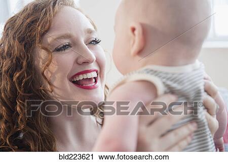 Stock Image - Caucasian woman holding baby son face to face. Fotosearch