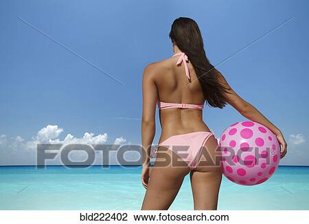Stock Image - Caucasian woman holding beach ball at ocean. Fotosearch
