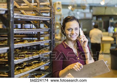 Picture - Caucasian woman holding clipboard using telephone in bakery. Fotosearch