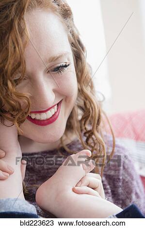 Stock Image - Caucasian woman holding foot of baby son. Fotosearch