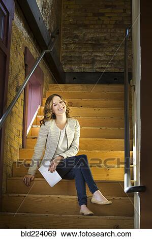 Caucasian woman holding paperwork sitting on wooden staircase View Large Photo Image Stock Photo - Caucasian woman holding paperwork sitting on wooden staircase. Fotosearch