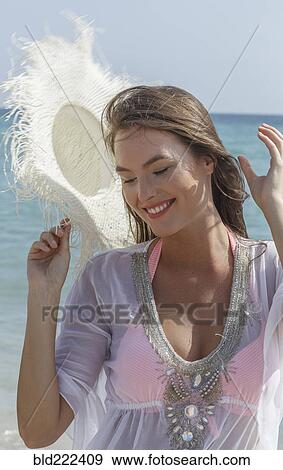 Stock Photo - Caucasian woman holding sun hat at beach. Fotosearch