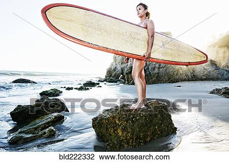 Stock Image - Caucasian woman holding surfboard at beach. Fotosearch