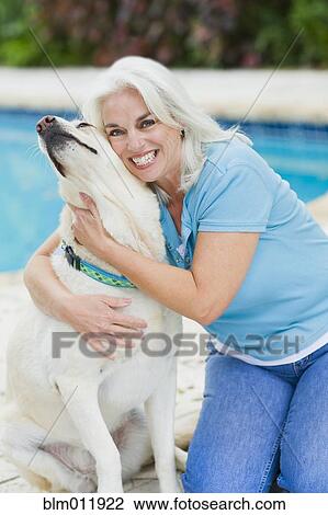 Stock Image - Caucasian woman hugging dog at poolside. Fotosearch