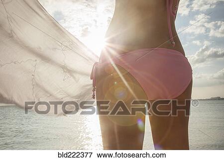 Stock Photo - Caucasian woman in bikini holding fabric at beach. Fotosearch