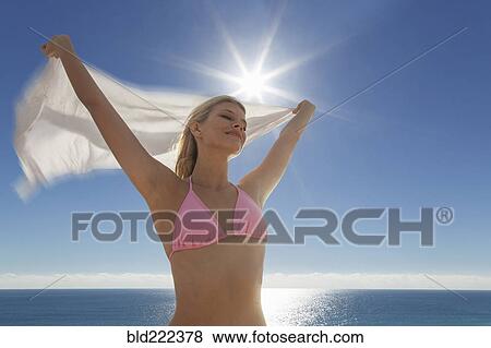 Stock Photo - Caucasian woman in bikini holding fabric at beach. Fotosearch