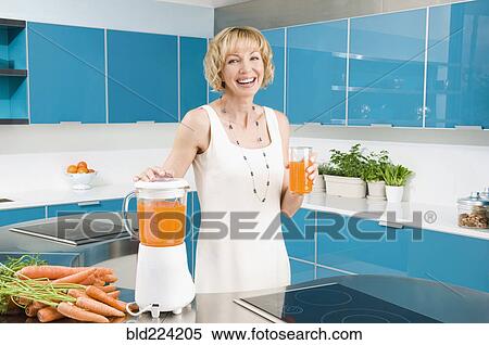Stock Photography - Caucasian woman juicing carrots in kitchen. Fotosearch