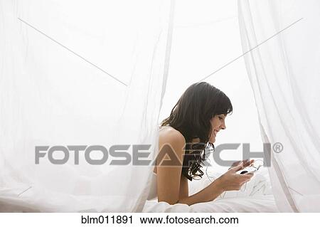Stock Image - Caucasian woman laying in bed listening to mp3 player. Fotosearch