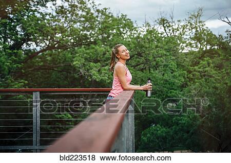Stock Photo - Caucasian woman leaning on banister holding water bottle. Fotosearch