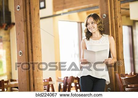 Stock Photo - Caucasian woman leaning on beam in cafe holding menu. Fotosearch