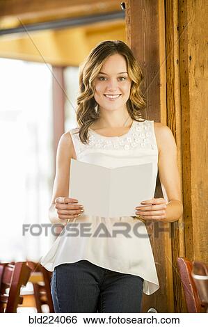 Stock Photograph - Caucasian woman leaning on beam in cafe holding menu. Fotosearch