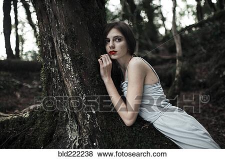 Stock Photo - Caucasian woman leaning on tree in forest. Fotosearch