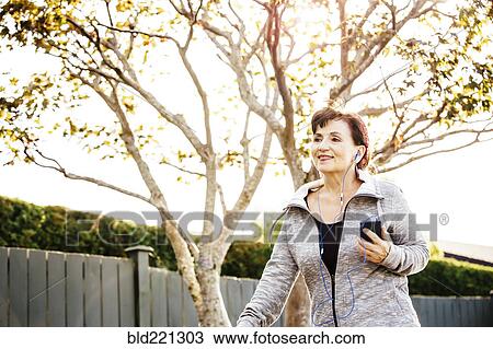 Stock Image - Caucasian woman listening to earbuds outdoors. Fotosearch