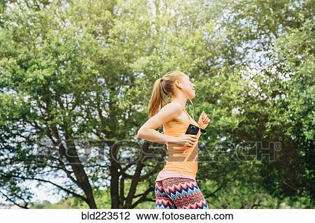 Stock Image - Caucasian woman listening to earbuds while running. Fotosearch
