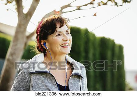 Stock Photograph - Caucasian woman listening to earbuds outdoors. Fotosearch