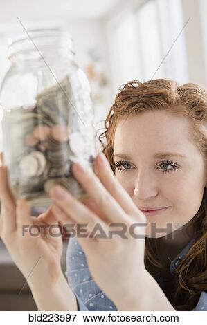 Caucasian woman looking at money in savings jar View Large Photo Image Stock Photo - Caucasian woman looking at money in savings jar. Fotosearch