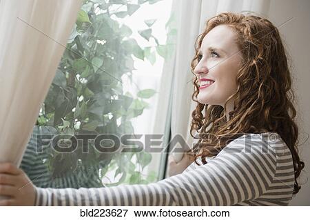 Stock Photo - Caucasian woman opening curtains at window. Fotosearch