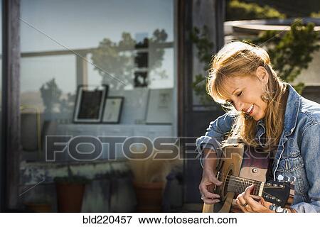 Stock Photo - Caucasian woman playing guitar on porch. Fotosearch