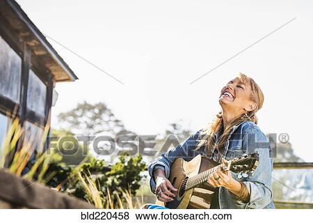 Stock Photo - Caucasian woman playing guitar on porch. Fotosearch