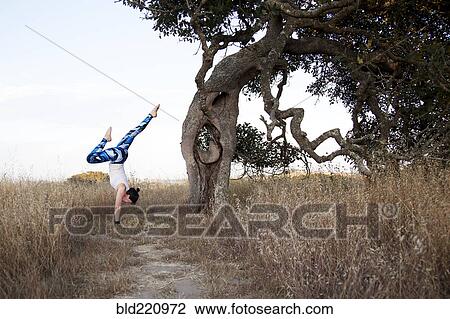 Stock Image - Caucasian woman practicing yoga in field. Fotosearch
