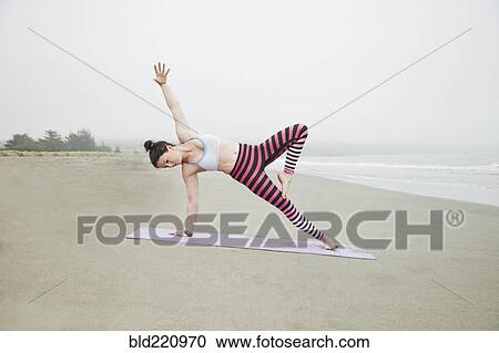 Stock Image - Caucasian woman practicing yoga on beach. Fotosearch