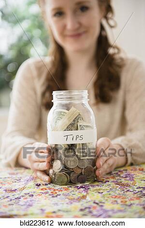 Stock Image - Caucasian woman showing money in tip jar. Fotosearch