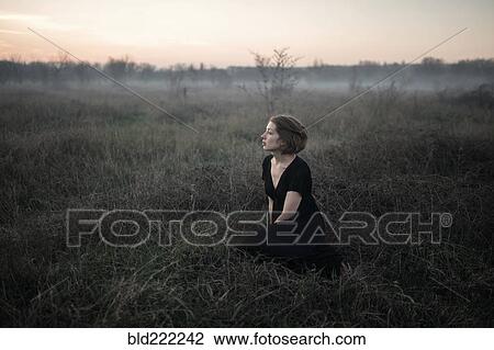 Stock Image - Caucasian woman sitting in remote field. Fotosearch