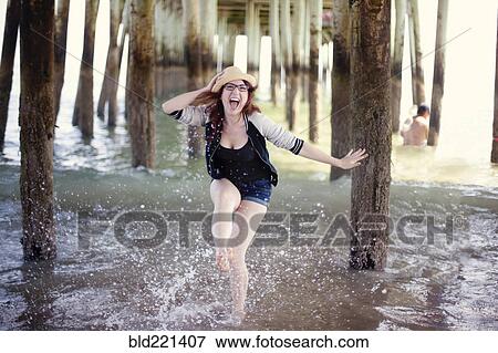 Stock Photo - Caucasian woman splashing in ocean under boardwalk. Fotosearch
