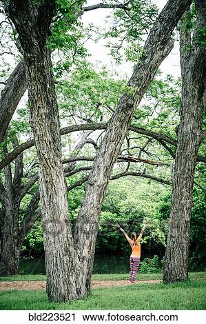 Stock Image - Caucasian woman standing with arms raised in park. Fotosearch