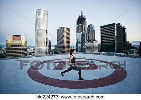 Stock Image - Caucasian woman stretching legs on urban rooftop. Fotosearch