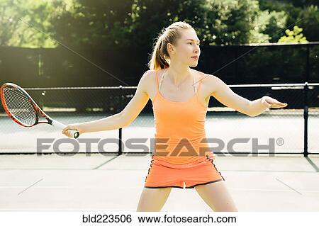 Stock Photograph - Caucasian woman swinging tennis racket on tennis court. Fotosearch